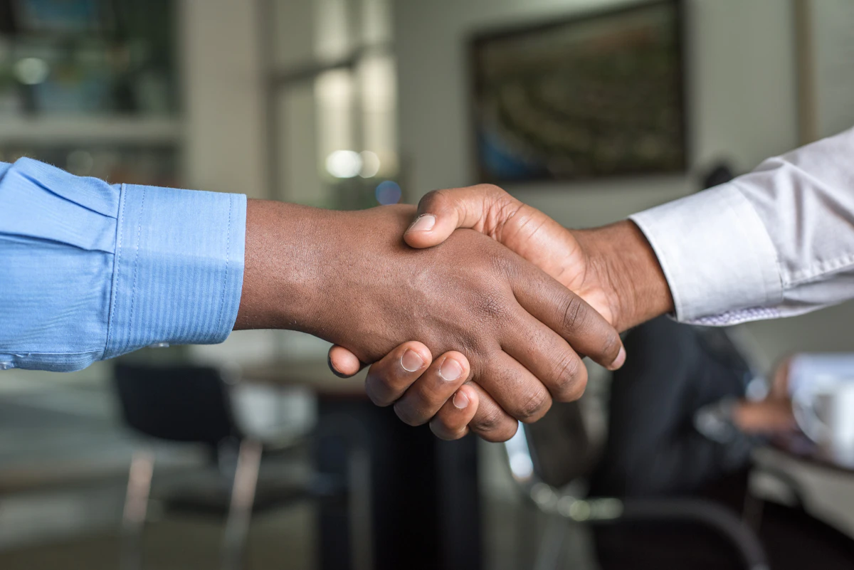 Two professionals shaking hands across a desk in a meeting